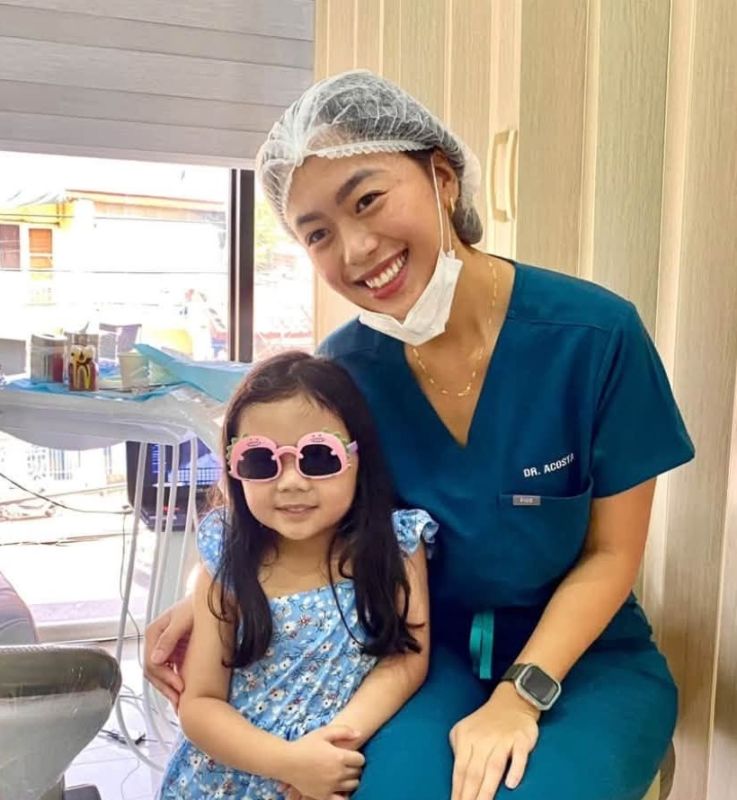 A dentist at Denta Cure Dental Clinic smiling beside a young patient