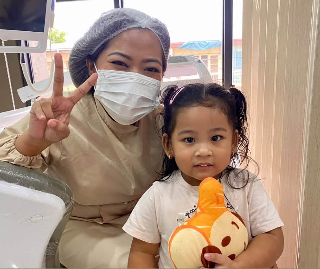 A young patient holding a stuffed toy beside her dentist at Denta Cure Dental Clinic